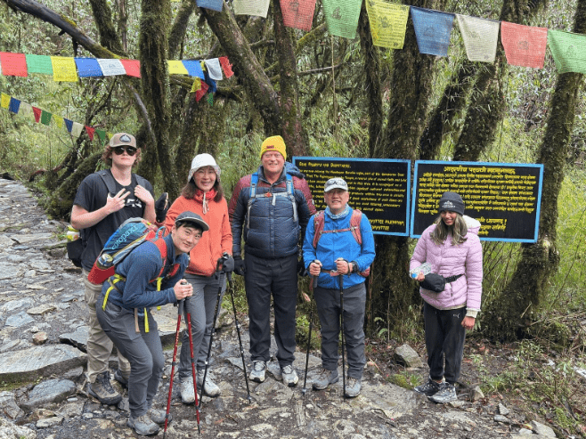 Group of Annapurna trekkers pause near prayer flags on the forest trail during the cancer equity trek.